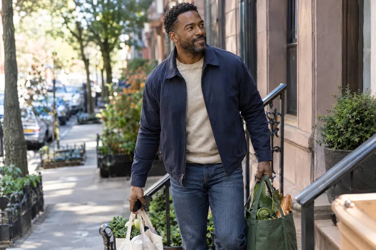 A man walking up the front steps of a city apartment building carrying two grocery bags.